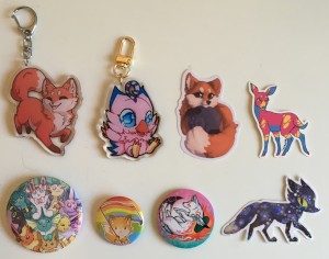 stickers: fox, night sky fox, pansexual deer; pins: Eevee variations, small fox with rainbow flag, Amaterasu; charms: fox, Biyomon